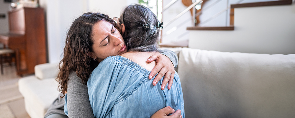 Adult female child hugs her senior mother.